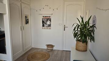 A hallway with a white door, a poster on the wall, a plant on a table, and a woven mat on the floor.