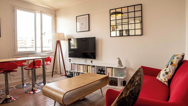 A modern living room with a red sofa, a wooden bench, a TV, a bookshelf, and a large window. - Spacious apartment near Père Lachaise (Paris)
