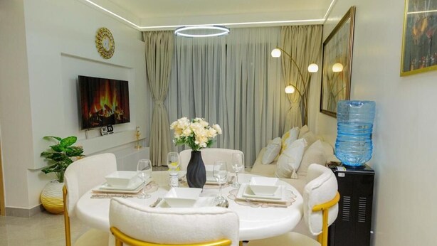 Een eethoek met een ronde tafel voor vier personen, witte stoelen, een vaas met bloemen en een waterdispenser.