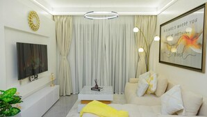 Een moderne woonkamer met een flatscreen televisie, een marmeren salontafel en een bank met decoratieve kussens.
