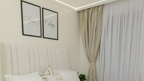 Een net opgemaakt bed met witte lakens en kussens, een hoofdbord, en twee ingelijste motiverende citaten aan de muur.