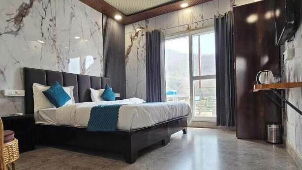 Ein modernes Schlafzimmer mit einem großen Bett, einem Holznachttisch, einem Korbstuhl und Blick ins Freie durch ein großes Fenster.