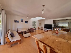 A spacious living area with a wooden dining table, a sofa, and a TV.