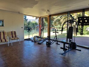 A spacious indoor gym with various exercise equipment, large windows, and a view of greenery outside.