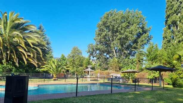 Piscina cercada por uma grade, com palmeiras e um gazebo ao fundo.