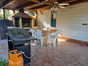 Une terrasse extérieure équipée d’un barbecue, de chaises et d’un ventilateur de plafond.