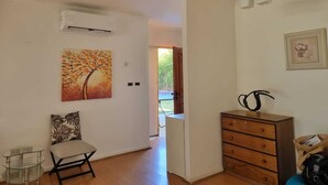 Quarto com cômoda de madeira, uma cadeira, ar condicionado e um quadro na parede.