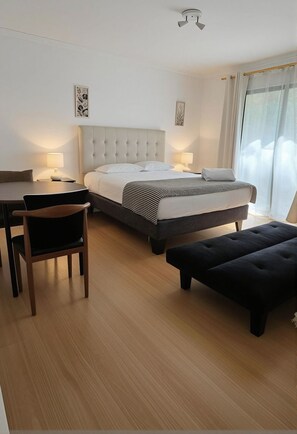 Hotellihuone, jossa on sänky, yöpöydät, tuoli, rahi ja kattotuuletin.
