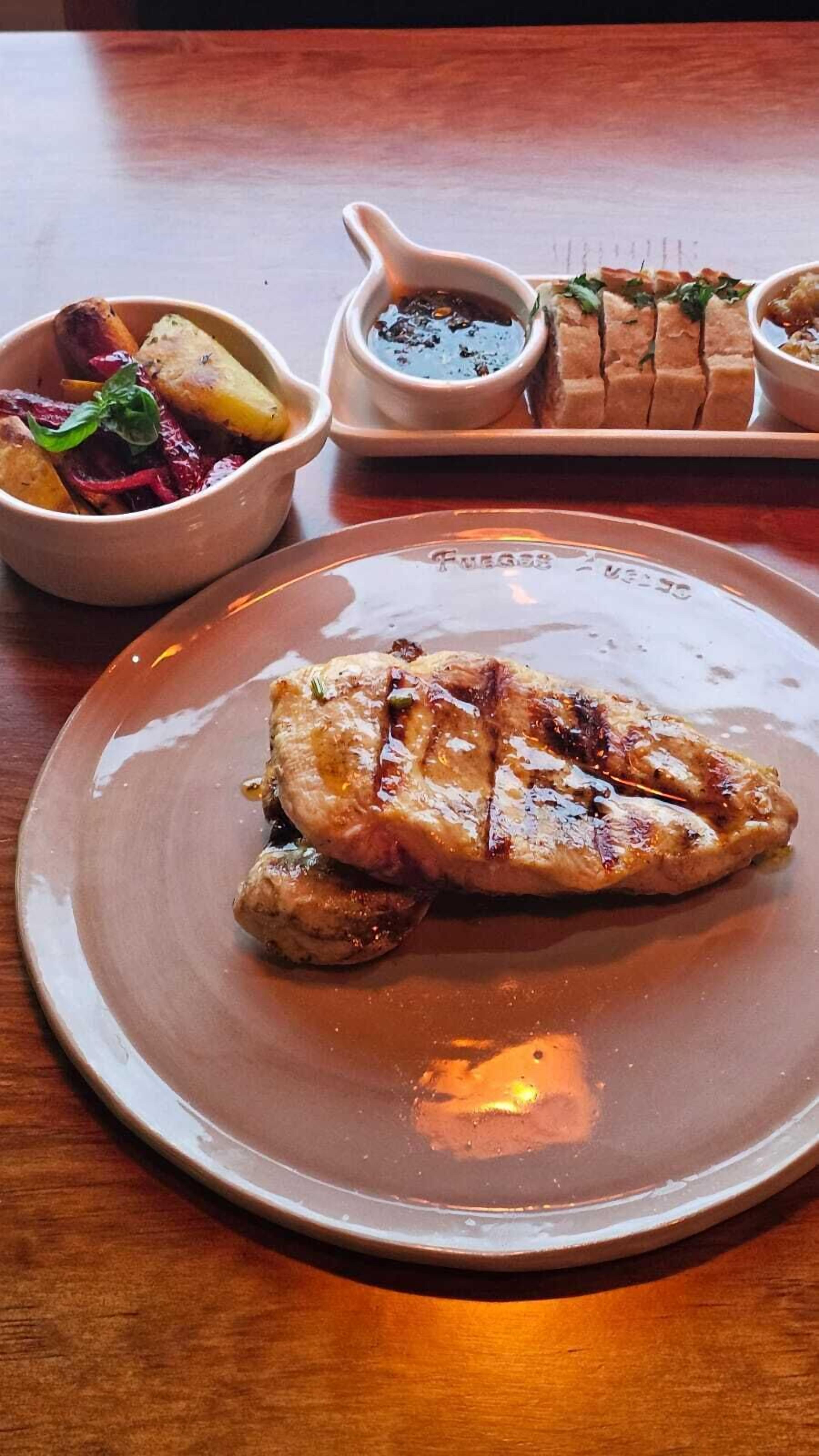 Un plato con carne a la parrilla, un bol de vegetales asados y una salsera pequeña.
