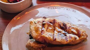 Un plato con carne a la parrilla, un bol de vegetales asados y una salsera pequeña.
