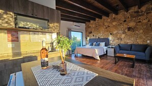 A modern room with a stone wall, a bed, a sofa, a table with a bottle and a plant, and a window with a view. - Rincon Del Malbec (Luján de Cuyo)