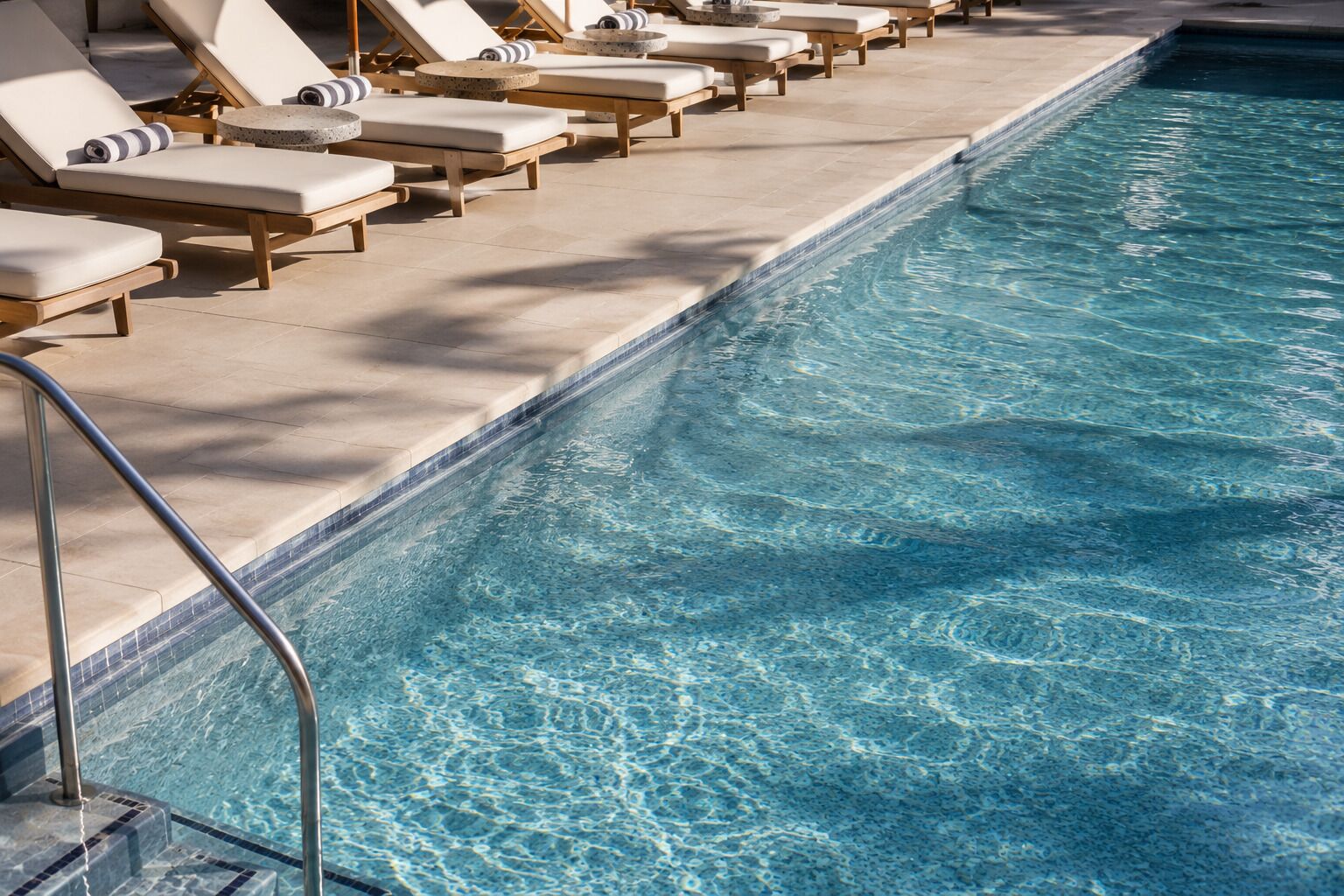 A swimming pool with lounge chairs and a tiled deck.