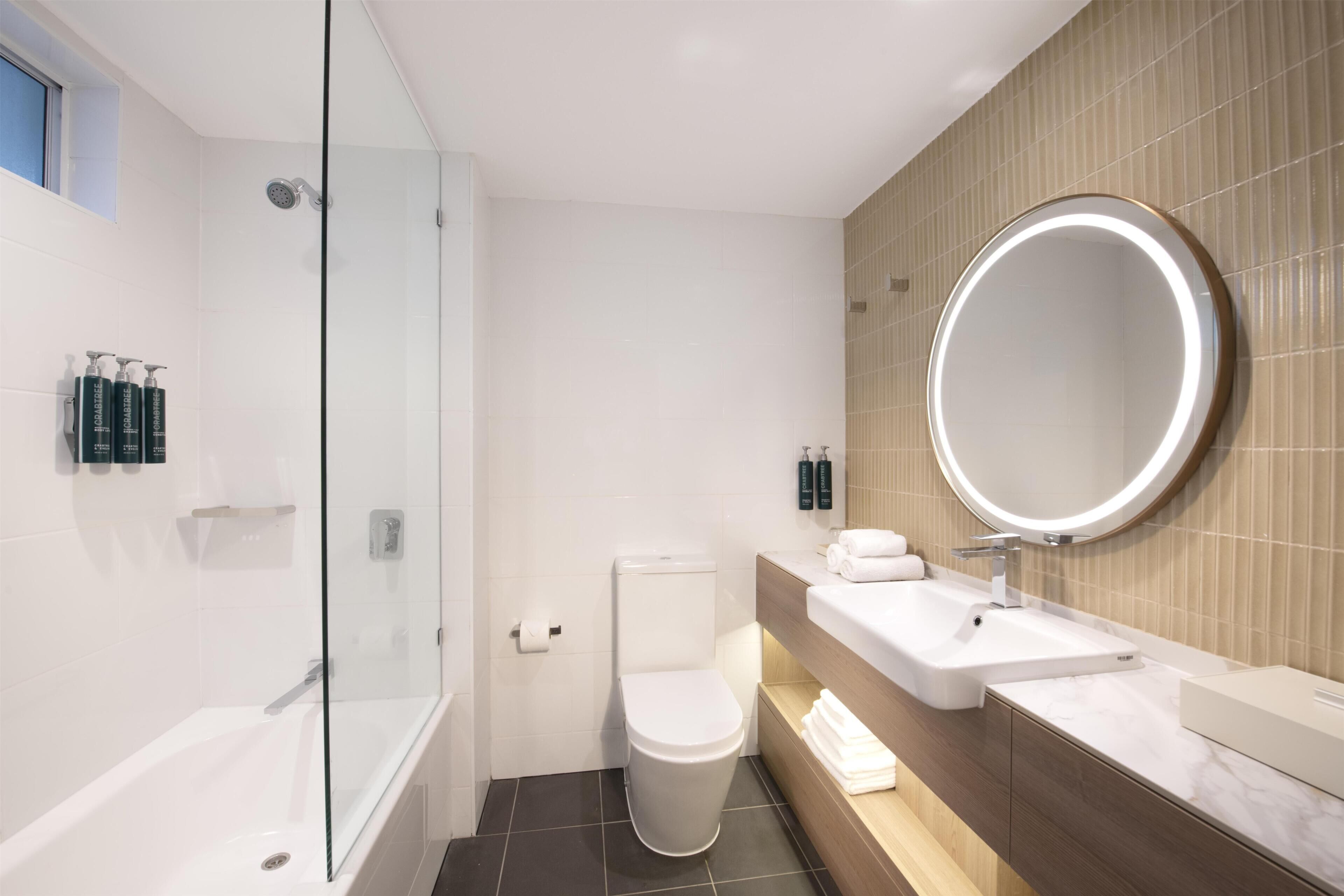 A modern bathroom with a glass-enclosed shower, a toilet, a sink with a mirror, and toiletries on the wall.