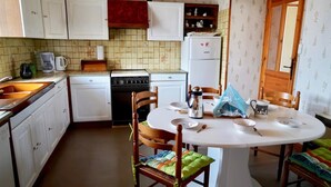 A compact kitchen with white cabinets, a stove, a refrigerator, and a dining table with chairs. - Holiday Home 'Les Cousines' with Mountain View, Private Terrace and Wi-Fi (Lavoûte-Chilhac)