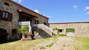A stone building with a staircase leading to a porch, surrounded by a grassy area. - Holiday Home 'Les Cousines' with Mountain View, Private Terrace and Wi-Fi (Lavoûte-Chilhac)