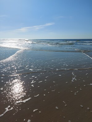 A beach with waves, clear sky, and sunlight reflecting on the sand. - Holiday Home “Petite Villa by the Sea” with Private Terrace and Garden (Soulac-sur-Mer)