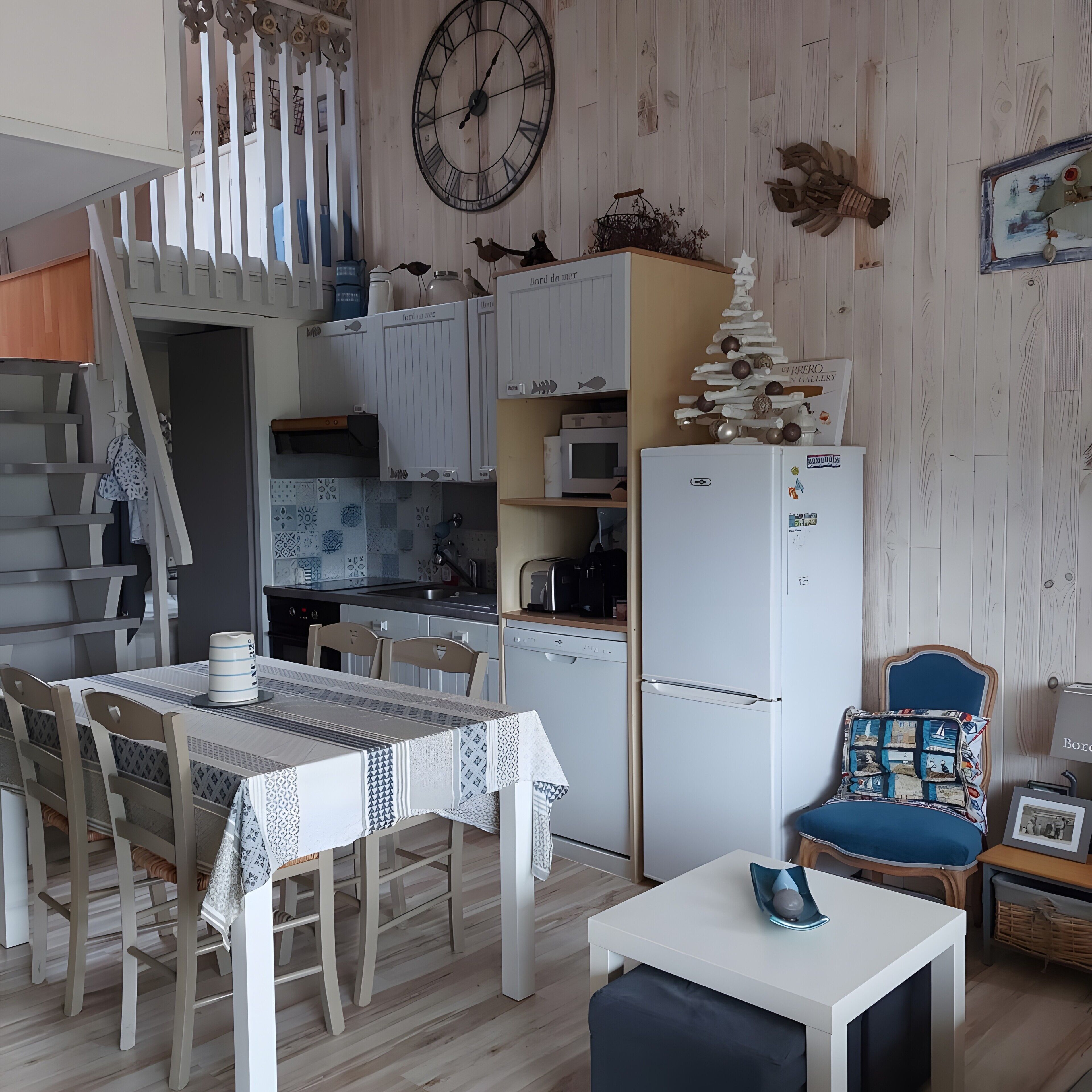 A kitchen with a clock, cabinets, a refrigerator, and a dining area with a table and chairs.