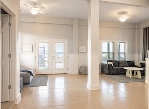 A spacious living area with a large window, a sofa, a coffee table, and a ceiling fan. - Steps to Gulf Beach & Private Lagoon + Amenities (Gulf Shores)