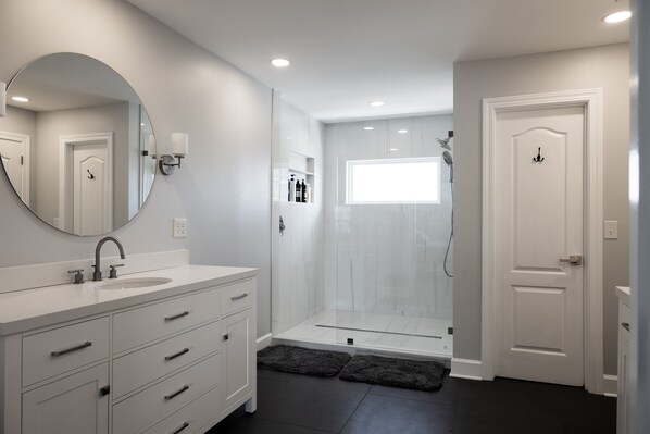 A modern bathroom with a large mirror, a sink, a shower, and a door. - Steps to Gulf Beach & Private Lagoon + Amenities (Gulf Shores)