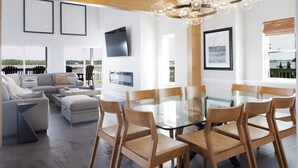 A modern living room with a glass dining table, wooden chairs, a sofa, and a TV mounted on the wall.