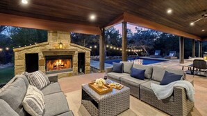 An outdoor living area with a stone fireplace, a pool, and a covered seating area.