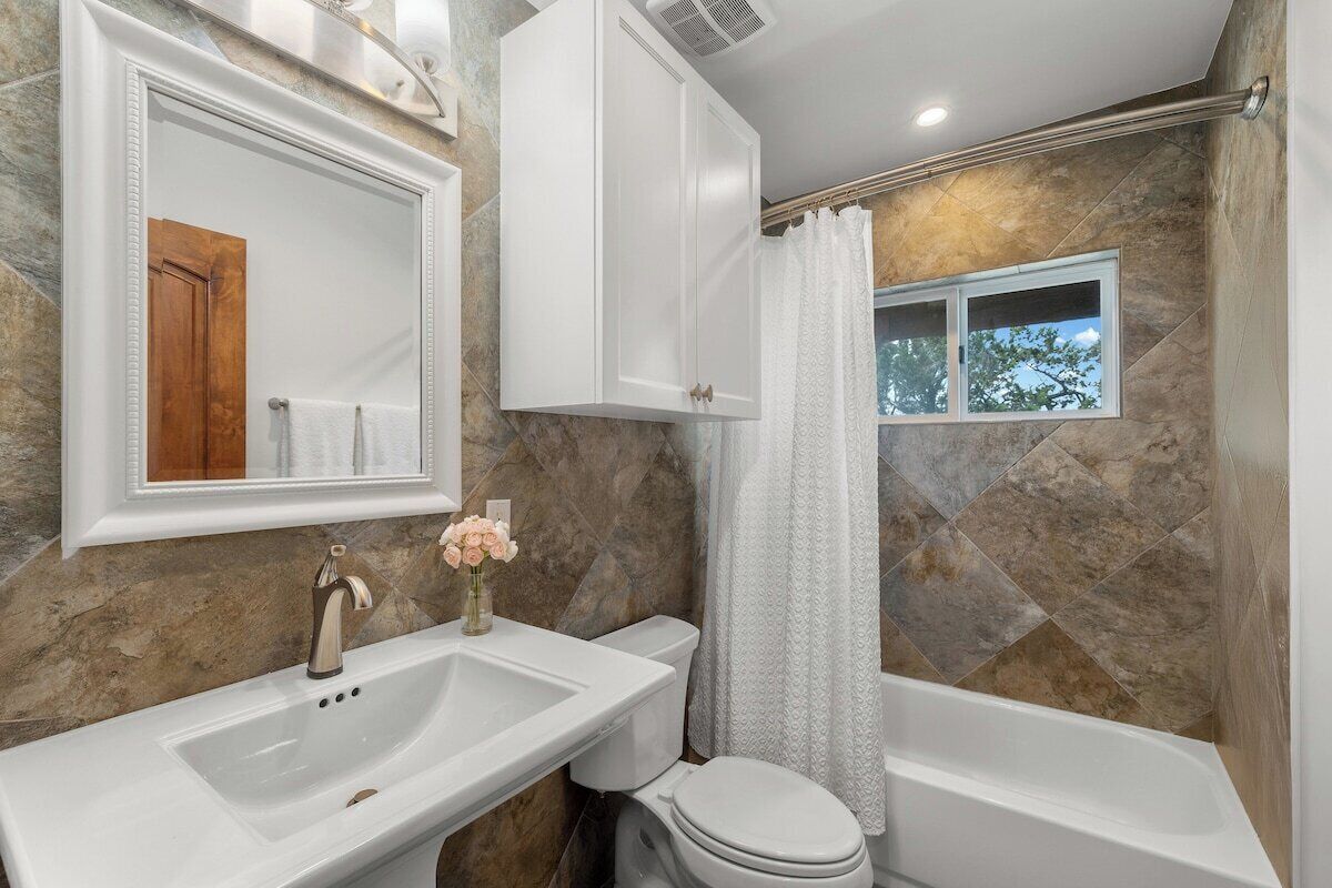A bathroom with a white sink, toilet, and bathtub. There is a window with a view of trees.