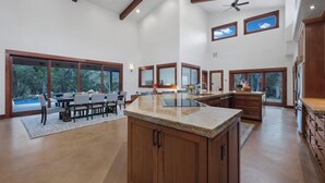 A spacious kitchen with a central island, large windows, and a dining area with a table and chairs.