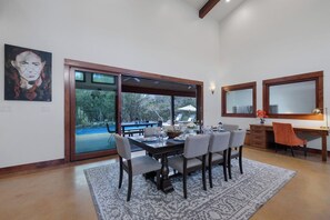 A dining area with a large table and chairs, a view of a pool, and a desk with a chair.