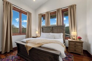 A bedroom with a large bed, two bedside tables with lamps, and curtains on the windows.