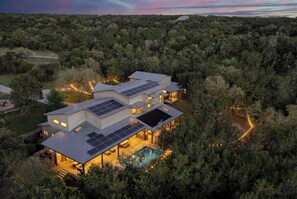A modern house with solar panels, a swimming pool, and surrounded by dense forest.