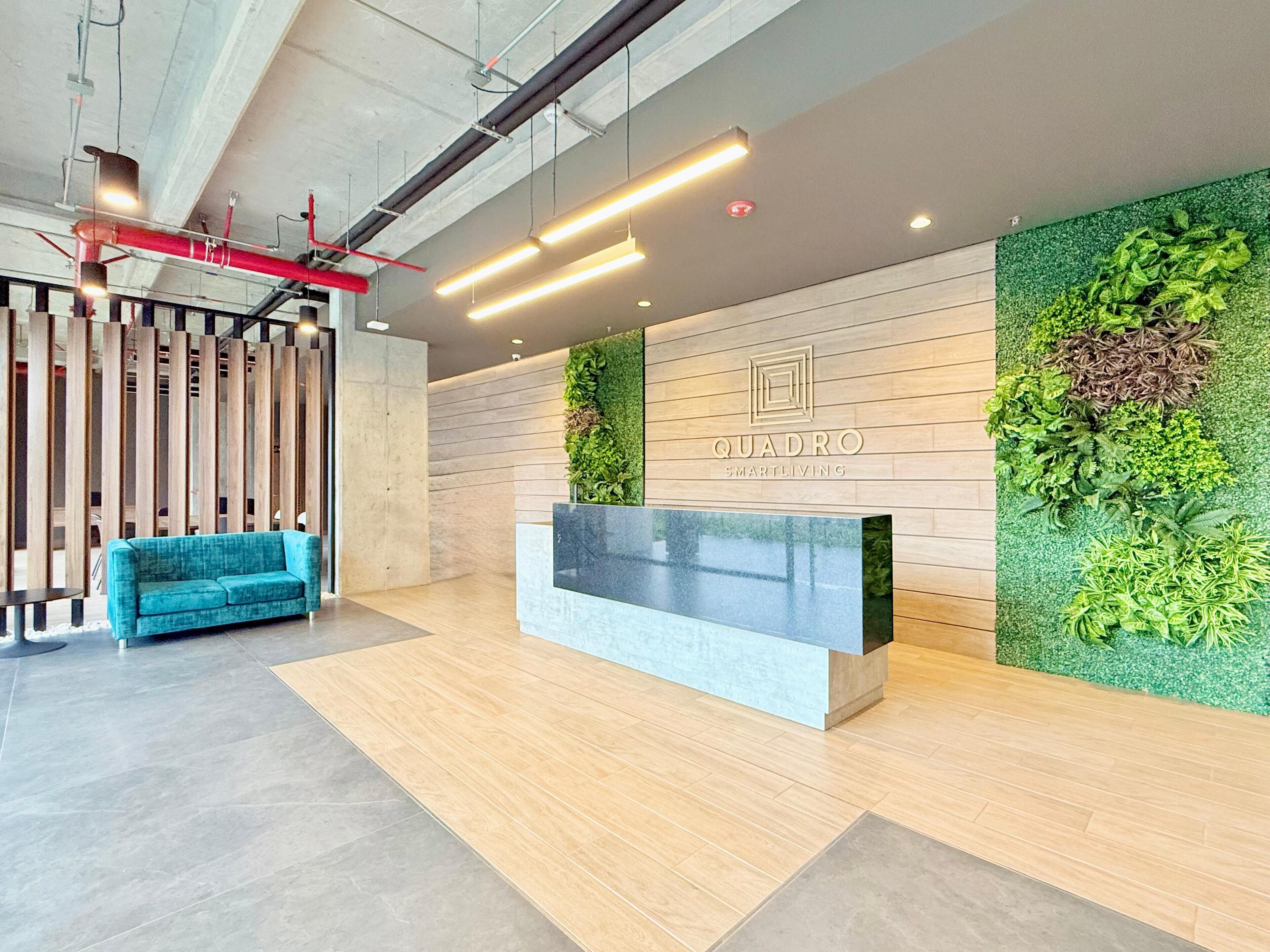 A modern reception area with a wooden reception desk, a blue sofa, and green vertical gardens.