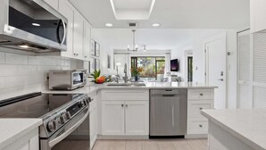 A modern kitchen with white cabinetry, stainless steel appliances, and a central island. - C-117 - Luxury Park Shore Resort Condo with Pool (Naples)