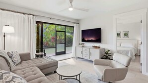 A modern living room with a sofa, armchair, and round coffee table, a TV mounted on the wall, and a sliding glass door leading to an outdoor area. - C-117 - Luxury Park Shore Resort Condo with Pool (Naples)