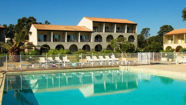 A swimming pool with lounge chairs and a building with arched windows in the background. - Apartment in Corsica Near Stunning Beach (Linguizzetta)