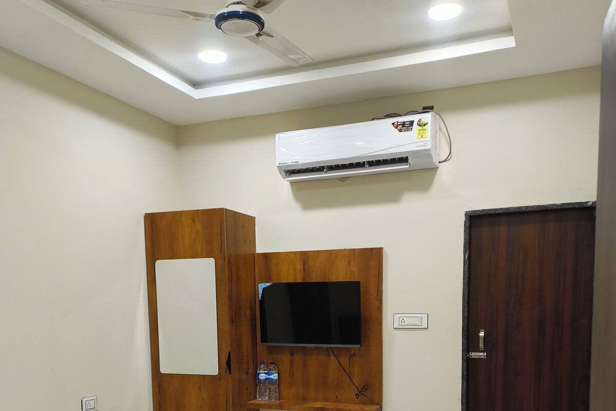 Slaapkamer met een bed, een houten garderobe, een wandgemonteerde televisie, een airconditioning en een deur.