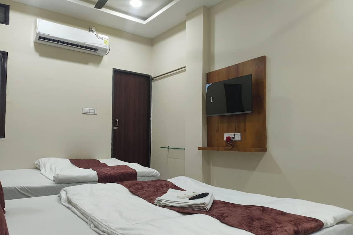 Een hotelkamer met twee bedden, een airconditioning, een houten plank met een televisie en een deur.