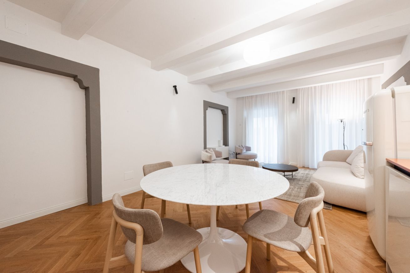 Ein modernes Wohnzimmer mit rundem Tisch, Stühlen, einer Couch und einem großen Spiegel.