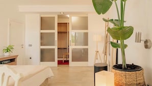 A modern bedroom with a bed, a bedside table, a potted plant, a floor lamp, and a wardrobe with frosted glass doors. - Maison du monde (Costa Adeje)