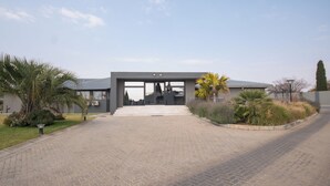 Un bâtiment moderne doté d’une entrée pavée, entouré de jardins aménagés et de palmiers.
