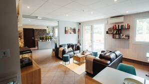 A spacious living area with a sofa set, a coffee table, and a dining table. There is a kitchen area in the background with a bookshelf and a window. - Cozy 2-bedroom Apartment for 4 People (Ax-les-Thermes)