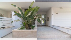 A modern building with a concrete staircase, a planter with large green leaves, and a white garage door. - Albamare (Alba Adriatica)