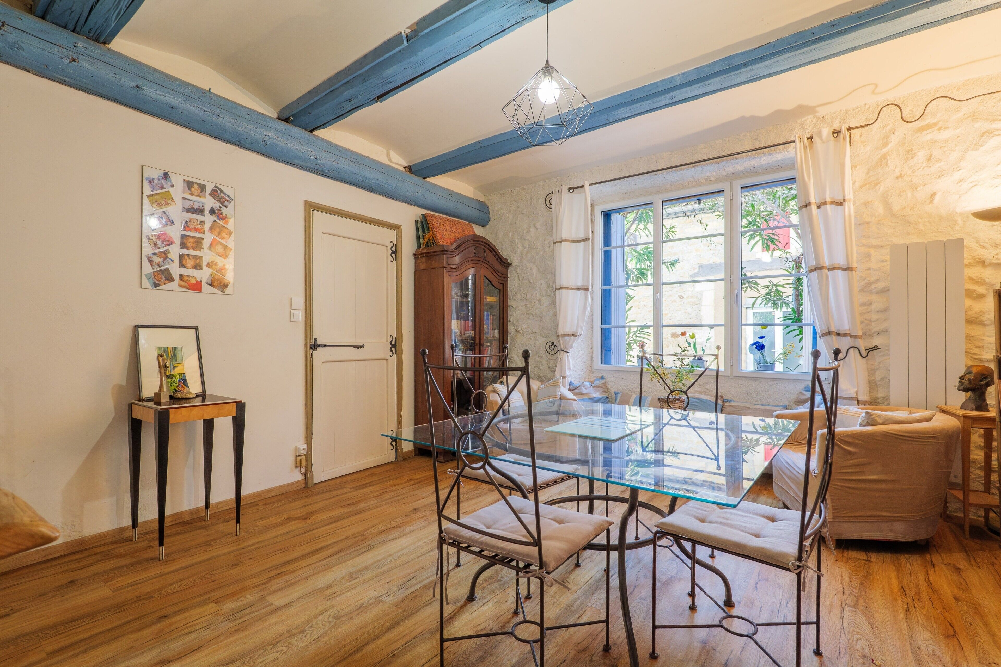 A dining area with a glass table and metal chairs, a wooden floor, a stone wall, and a window with curtains.