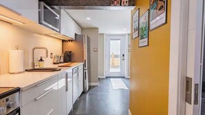 Een moderne keuken met witte kasten, roestvrijstalen apparatuur en een gele accentmuur.