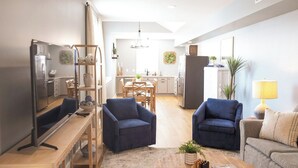 Uma sala de estar moderna com uma televisão, duas poltronas azuis, uma mesa de centro de madeira e um sofá.