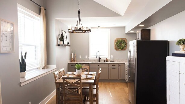 Uma cozinha moderna com uma mesa de jantar, cadeiras, um lustre e uma geladeira.