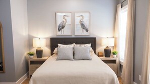 Quarto bem arrumado com uma cama grande, duas mesas de cabeceira com luminárias, uma cabeceira e duas obras de arte emolduradas na parede.