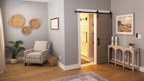 Um quarto com uma poltrona listrada, um banco com velas e uma porta que dá para outro aposento.