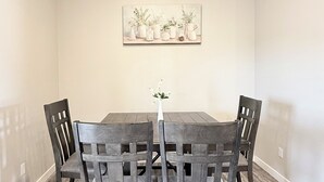 Ein Esszimmer mit einem Holztisch und Stühlen, einem Bild an der Wand und einer Vase mit Blumen auf dem Tisch.