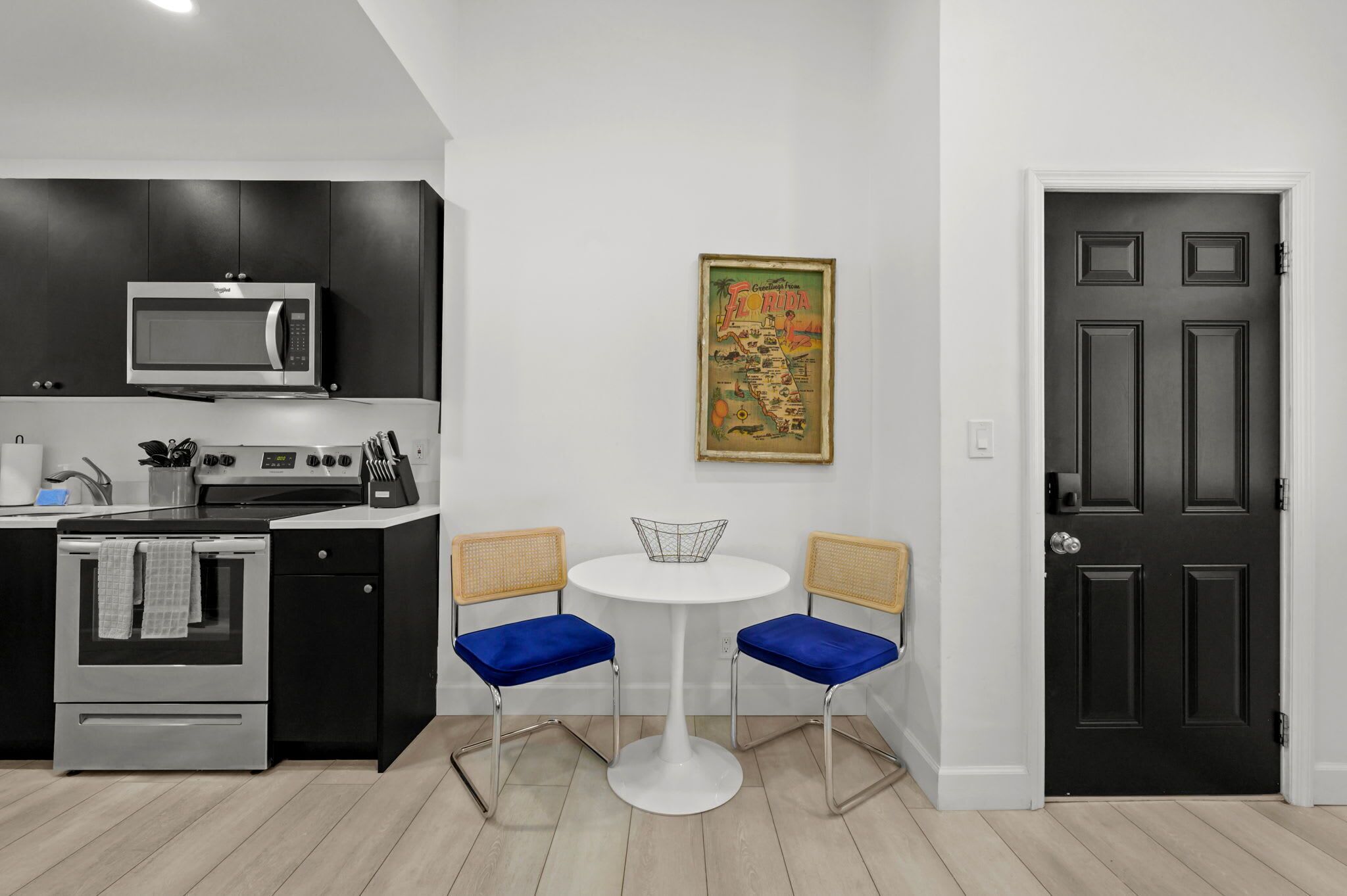 A modern kitchen with a microwave, oven, and dining area with two blue chairs and a white table.