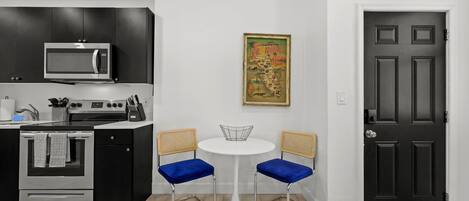 A modern kitchen with a microwave, oven, and dining area with two blue chairs and a white table.